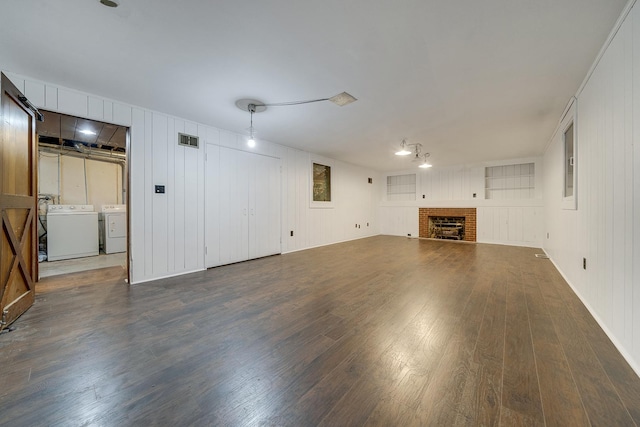 unfurnished living room featuring washer and dryer, a brick fireplace, wood finished floors, and visible vents