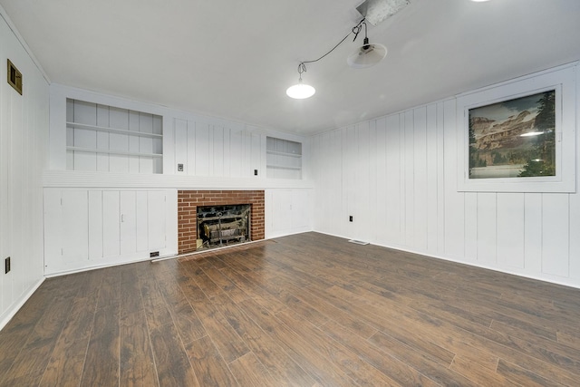 unfurnished living room featuring built in features, visible vents, a brick fireplace, and wood finished floors