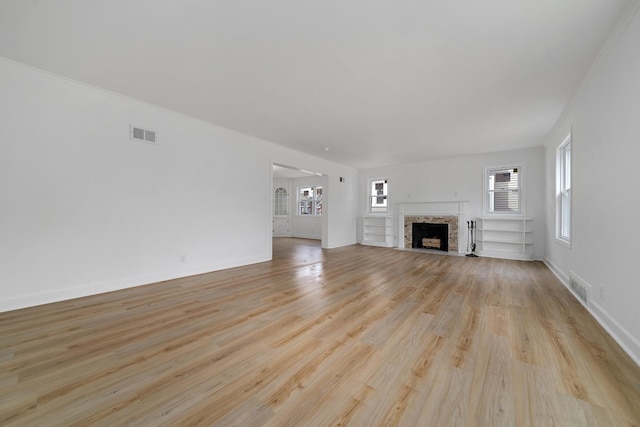 unfurnished living room with light wood-style flooring, a fireplace with flush hearth, baseboards, and visible vents