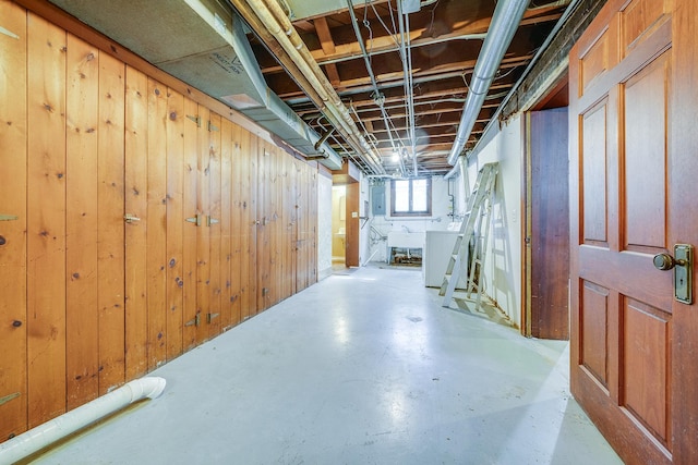 basement featuring electric panel, wooden walls, washer / dryer, and a sink