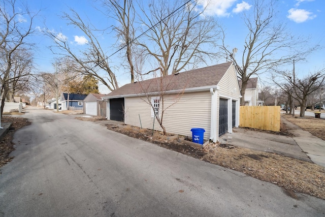 exterior space with a detached garage, a shingled roof, an outdoor structure, and fence