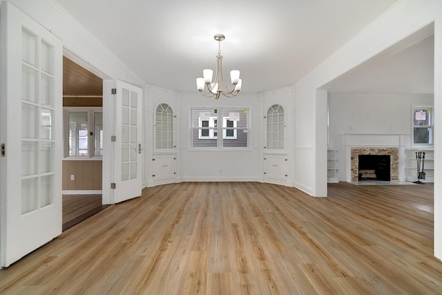 unfurnished living room featuring baseboards, an inviting chandelier, light wood-style flooring, a fireplace with flush hearth, and ornamental molding