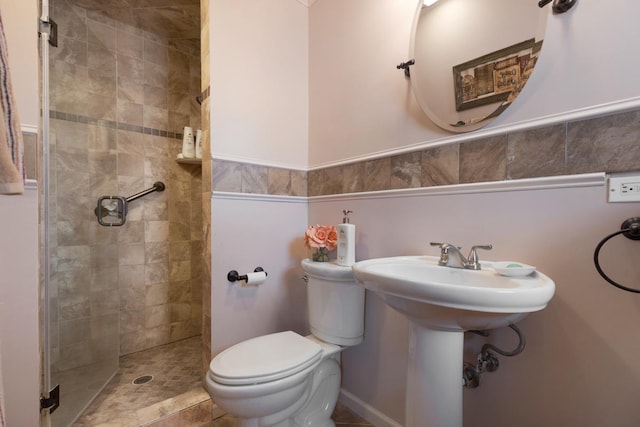 full bath featuring toilet, a stall shower, a sink, and wainscoting