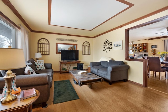 living room featuring ceiling fan, crown molding, baseboards, and wood finished floors