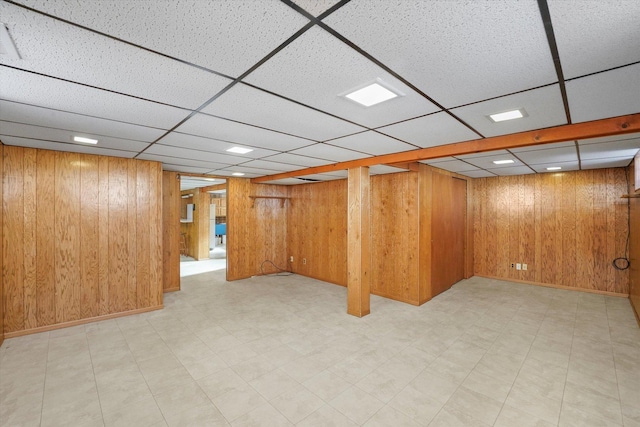 finished below grade area featuring a paneled ceiling, wooden walls, and light floors