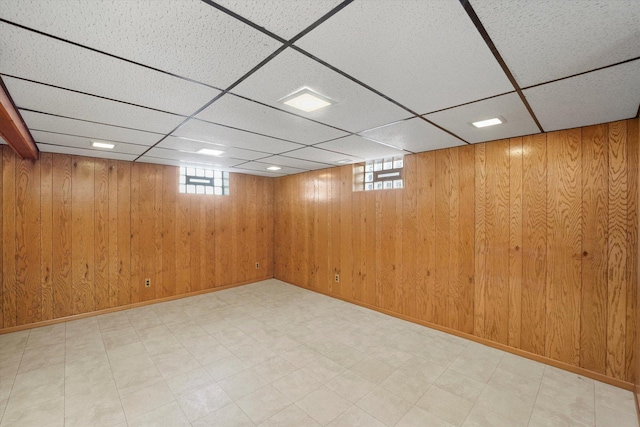 below grade area featuring a paneled ceiling, baseboards, wooden walls, and light floors