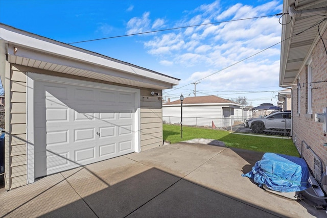 detached garage featuring concrete driveway and fence