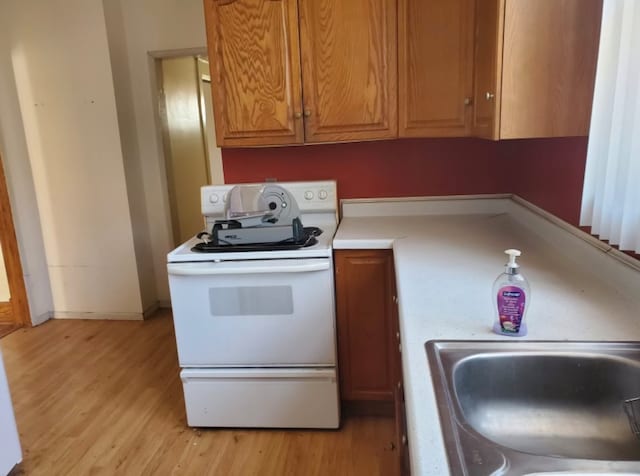 kitchen featuring light wood-style flooring, white range with electric cooktop, a sink, light countertops, and baseboards