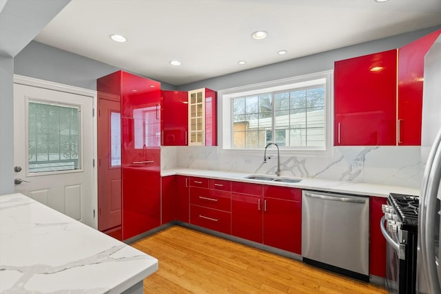 kitchen featuring stainless steel appliances, red cabinets, light wood finished floors, and a sink