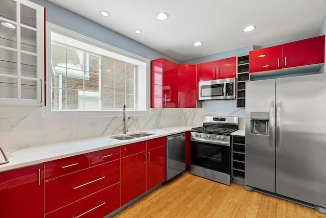 kitchen featuring light wood finished floors, appliances with stainless steel finishes, red cabinetry, and a sink