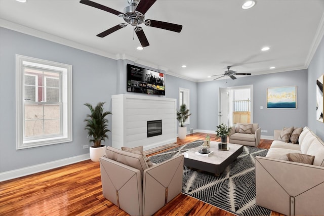 living room with ornamental molding, a glass covered fireplace, baseboards, and wood finished floors