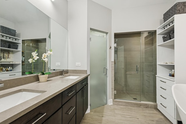 bathroom with double vanity, wood finished floors, a stall shower, and a sink