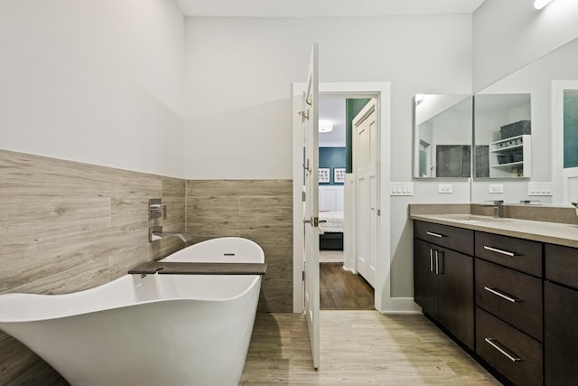 ensuite bathroom featuring wood finished floors, ensuite bathroom, vanity, a freestanding tub, and tile walls