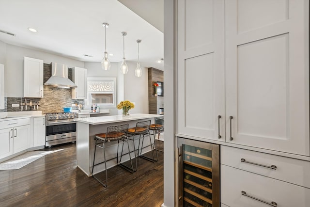 kitchen with wine cooler, backsplash, white cabinets, wall chimney range hood, and high end range