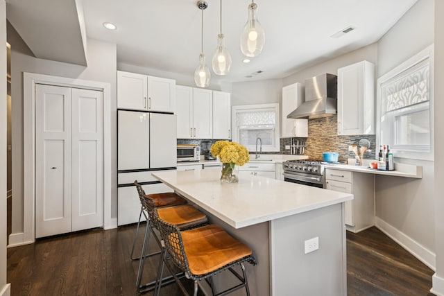 kitchen with freestanding refrigerator, a healthy amount of sunlight, stainless steel range, and wall chimney exhaust hood