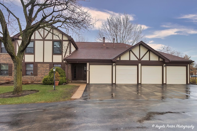 tudor home with a shingled roof, brick siding, a garage, and stucco siding