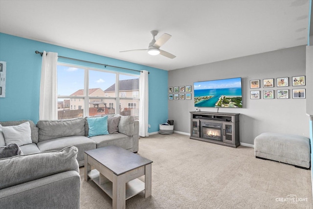 living area with a ceiling fan, a glass covered fireplace, baseboards, and carpet