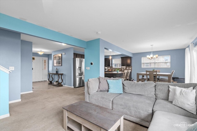 living area featuring light colored carpet, a notable chandelier, and baseboards