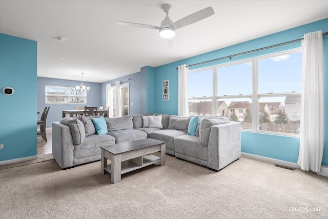 carpeted living room featuring ceiling fan with notable chandelier and baseboards