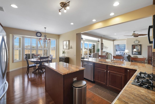 kitchen featuring a sink, dark wood finished floors, a center island, stainless steel appliances, and light stone countertops