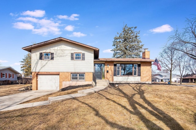 split level home featuring a garage, brick siding, concrete driveway, a chimney, and a front yard