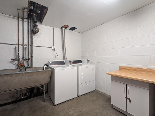 laundry room featuring cabinet space, concrete block wall, washing machine and dryer, and a sink