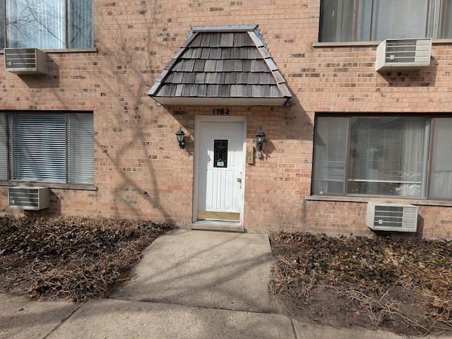 doorway to property with brick siding and a wall mounted AC