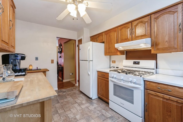 kitchen with white appliances, brown cabinetry, light countertops, and under cabinet range hood