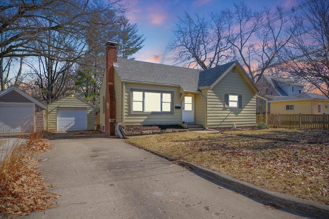 view of front facade with driveway, a detached garage, a chimney, an outbuilding, and fence