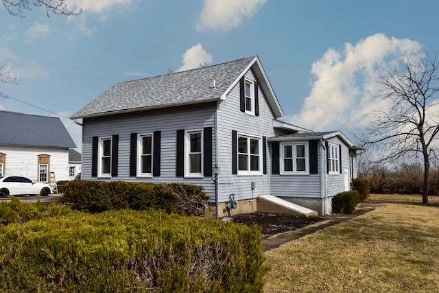 view of side of home with a shingled roof and a lawn