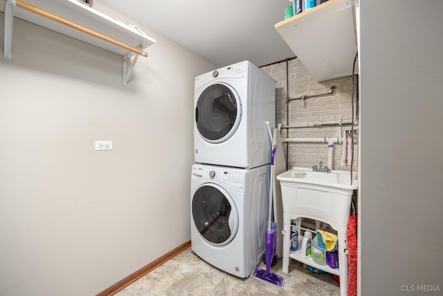 laundry room with laundry area, brick wall, baseboards, and stacked washer / dryer