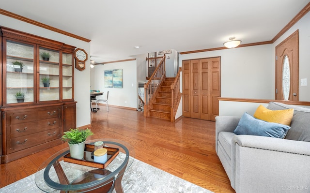 living room with light wood-style floors, ornamental molding, stairway, and baseboards