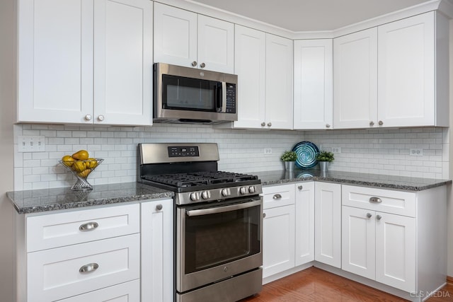 kitchen featuring dark stone counters, appliances with stainless steel finishes, light wood finished floors, and tasteful backsplash