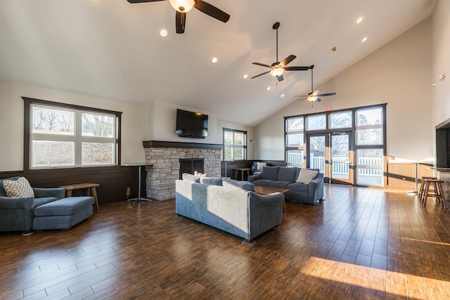 living area with ceiling fan, a stone fireplace, high vaulted ceiling, and dark wood-type flooring