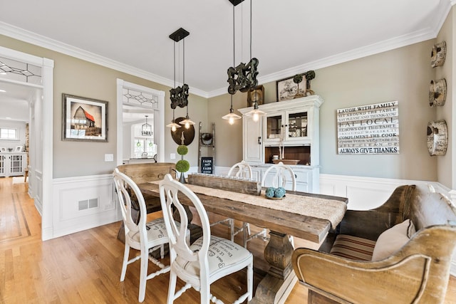 dining room with visible vents, wainscoting, light wood finished floors, ornamental molding, and a decorative wall