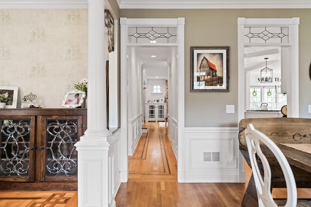 corridor featuring visible vents, ornamental molding, light wood-style floors, and a wainscoted wall