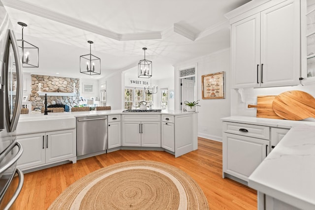 kitchen with a stone fireplace, crown molding, white cabinets, light wood-style floors, and stainless steel appliances