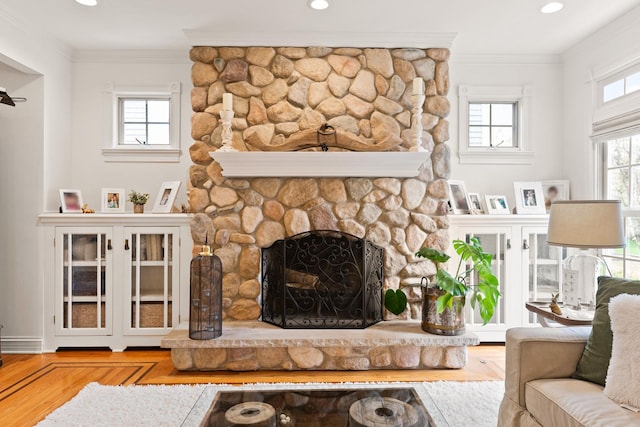 living area featuring ornamental molding, a stone fireplace, recessed lighting, and wood finished floors