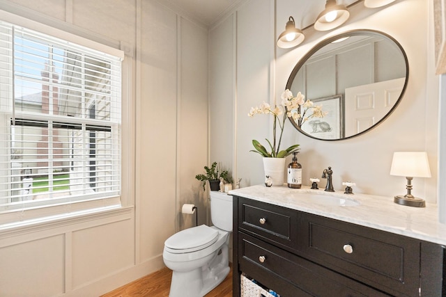 bathroom featuring crown molding, wood finished floors, vanity, toilet, and a decorative wall
