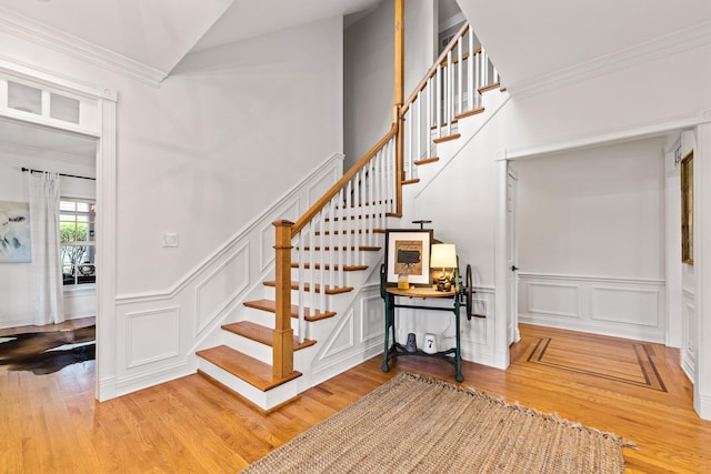 stairway with ornamental molding, wood finished floors, a decorative wall, a wainscoted wall, and vaulted ceiling