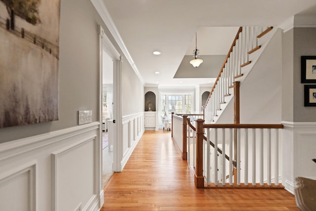hall featuring crown molding, arched walkways, a decorative wall, and light wood-style flooring