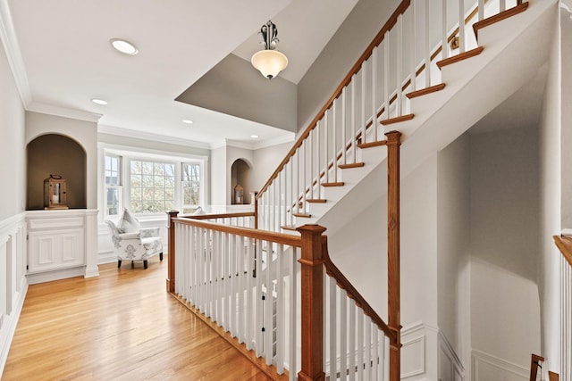 stairs with wood finished floors, a wainscoted wall, ornamental molding, a decorative wall, and recessed lighting