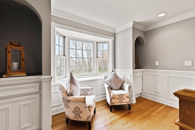 sitting room with crown molding, a decorative wall, arched walkways, a wainscoted wall, and light wood-type flooring