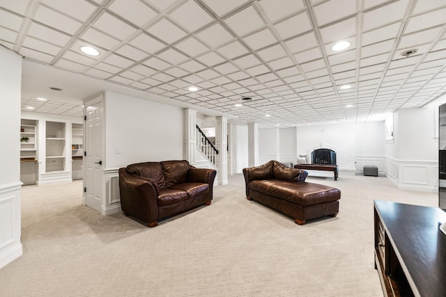 carpeted living room featuring stairs, a wainscoted wall, a fireplace with raised hearth, a decorative wall, and recessed lighting