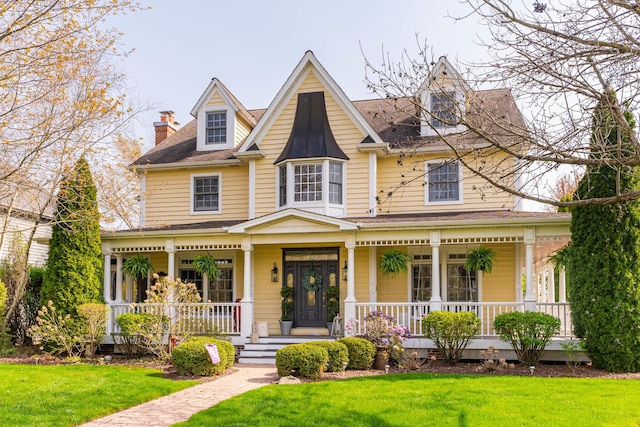 victorian house with a porch, a chimney, and a front yard