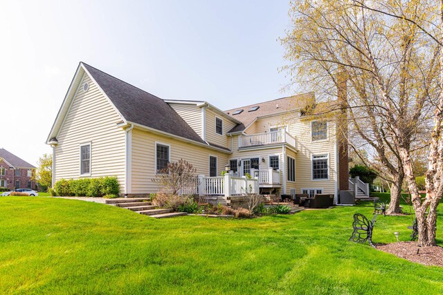 rear view of property featuring roof with shingles, a yard, a balcony, and a wooden deck