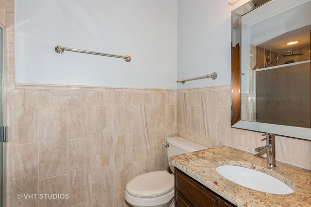 full bathroom with a shower with shower door, toilet, tile walls, wainscoting, and vanity