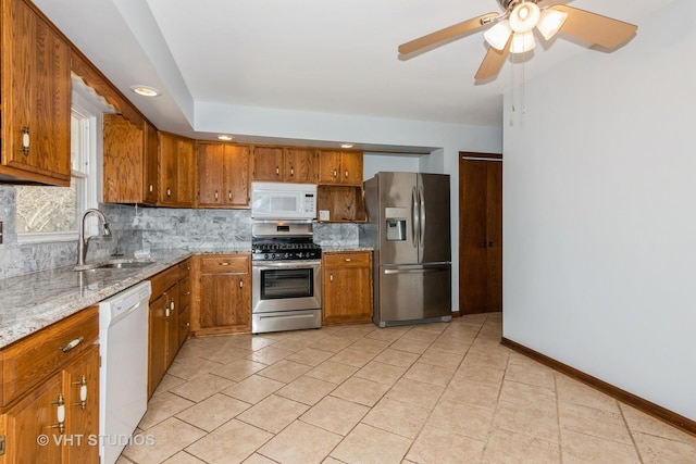 kitchen with tasteful backsplash, baseboards, appliances with stainless steel finishes, brown cabinetry, and a sink