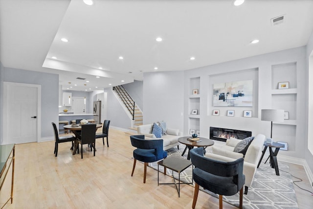 living room featuring visible vents, light wood-style floors, stairs, built in features, and a glass covered fireplace