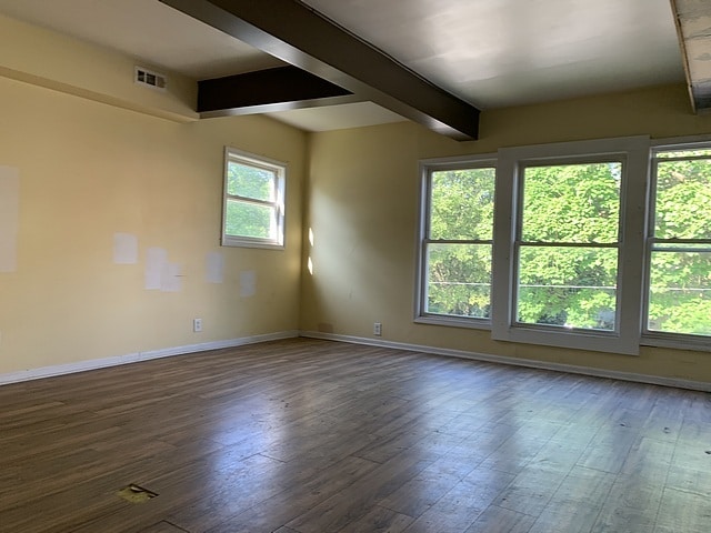 unfurnished room featuring dark wood-type flooring, beamed ceiling, visible vents, and baseboards